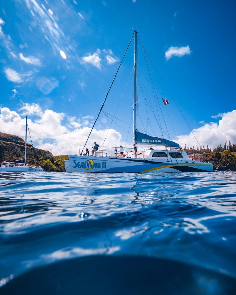 Sailboat with people on water, cloudy sky, and a distant shore.