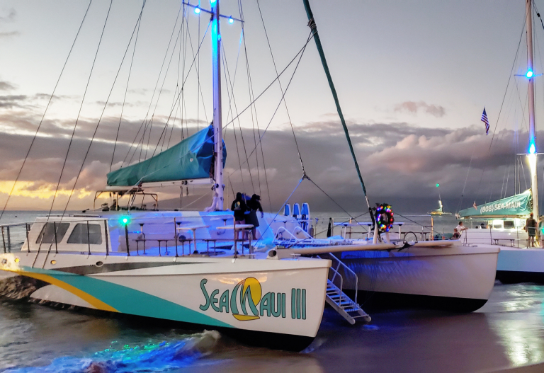 Two catamarans docked at sunset with a colorful sky background.