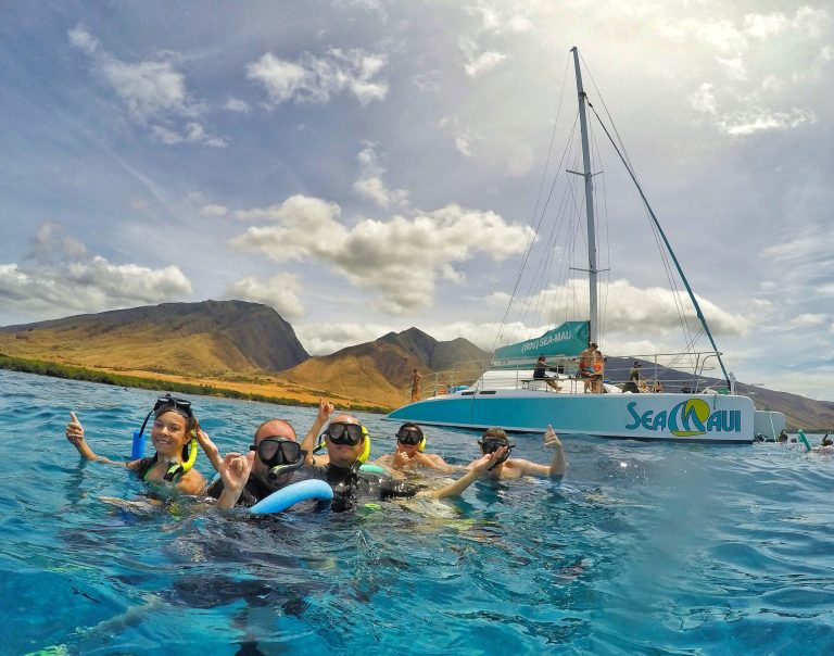 Group of snorkelers near a sailboat with mountains in the background.