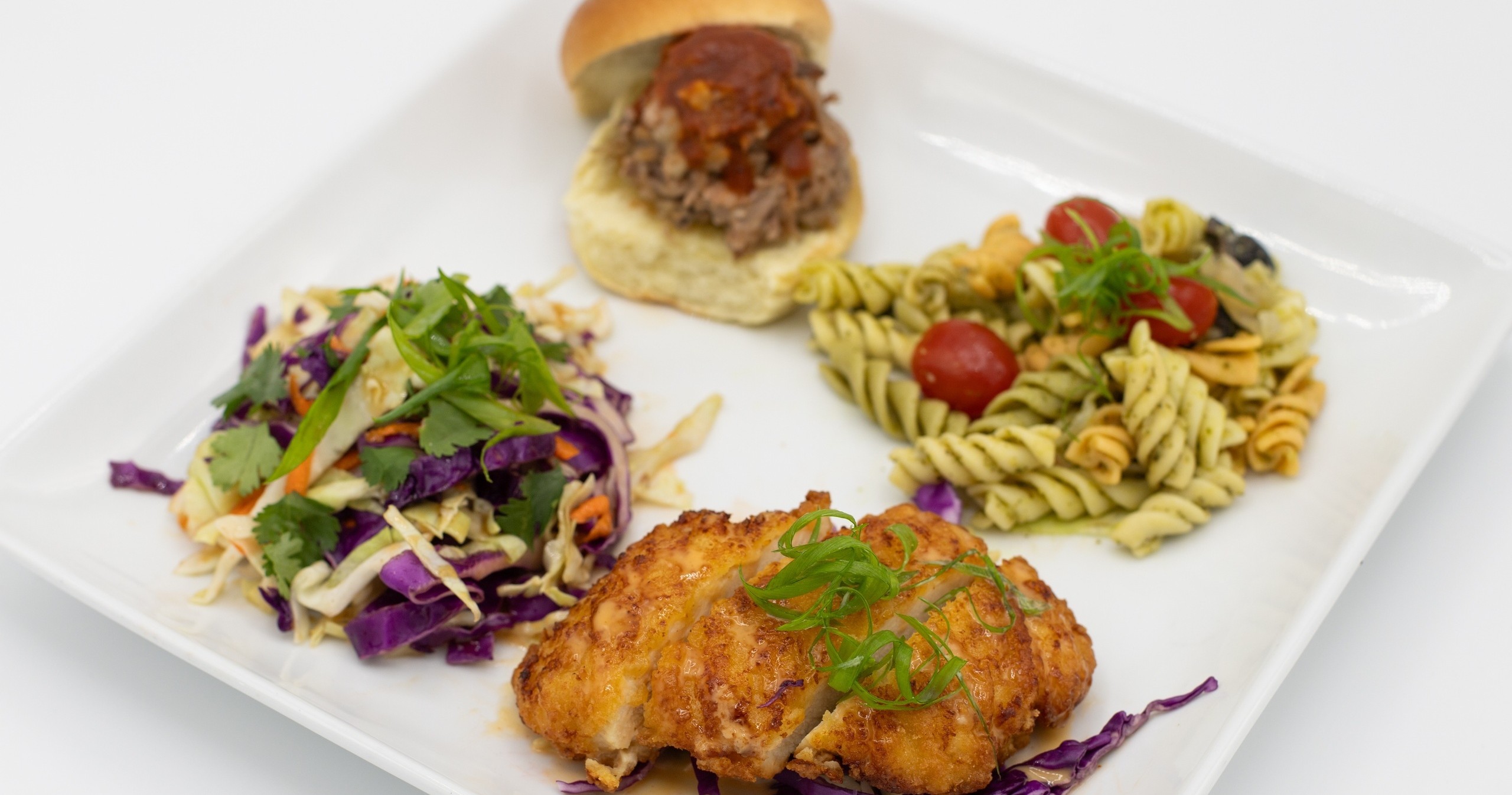 Plate with fried chicken, pasta salad, coleslaw, and a small meat sandwich.