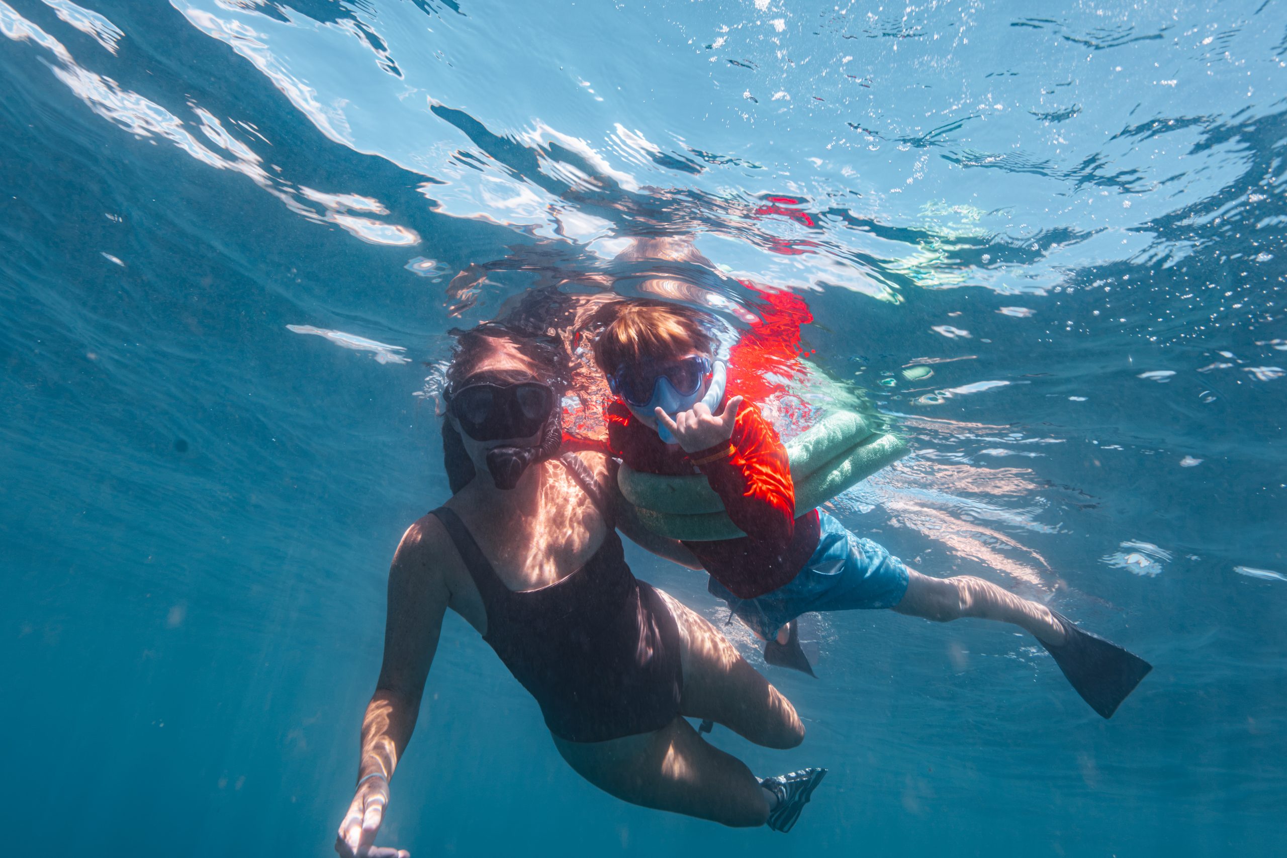 Two people snorkeling underwater in clear blue water.