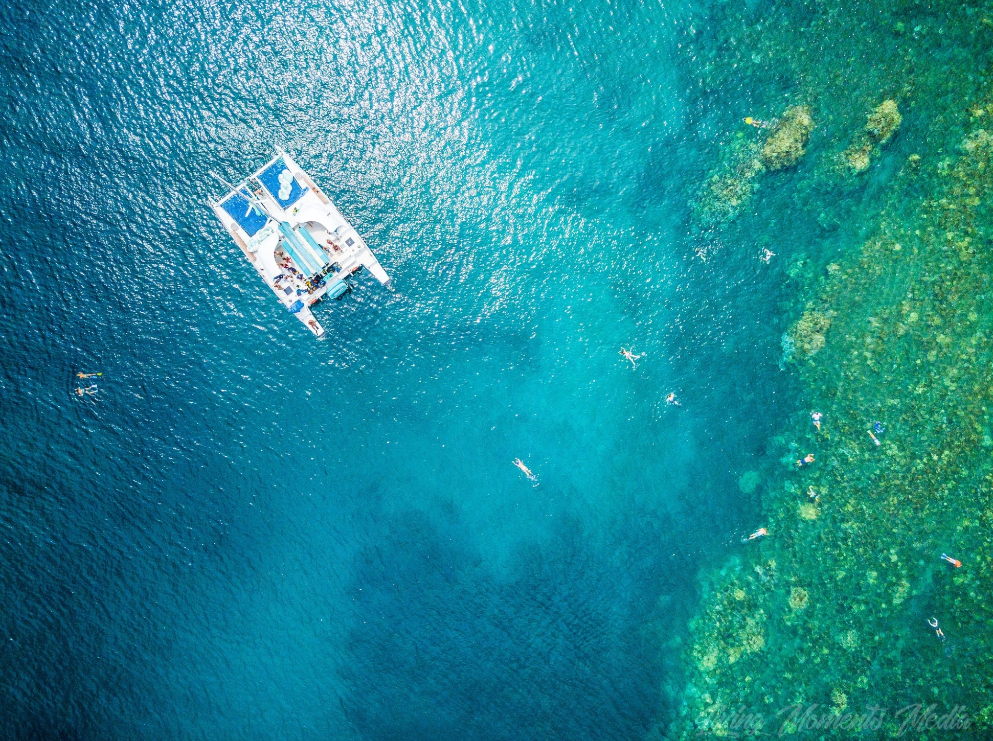 Aerial view of a catamaran and swimmers in clear blue water.