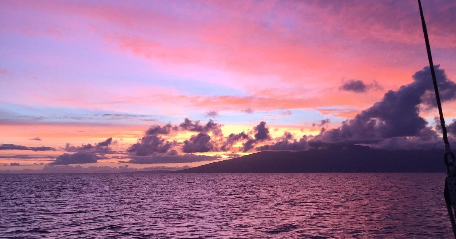 Colorful sunset over ocean with scattered clouds and silhouette of distant land.