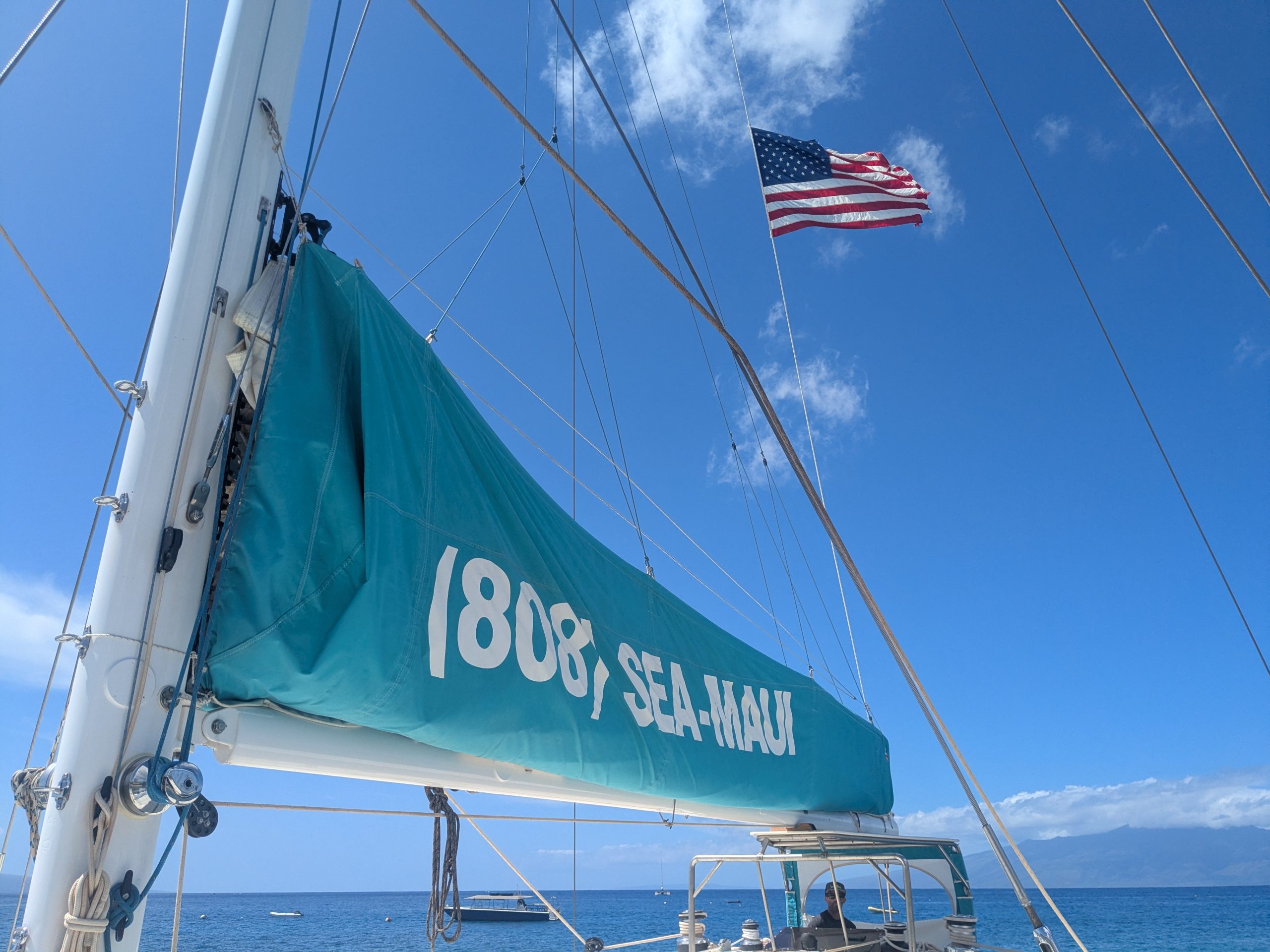 Sailboat with teal sail and USA flag against blue sky.