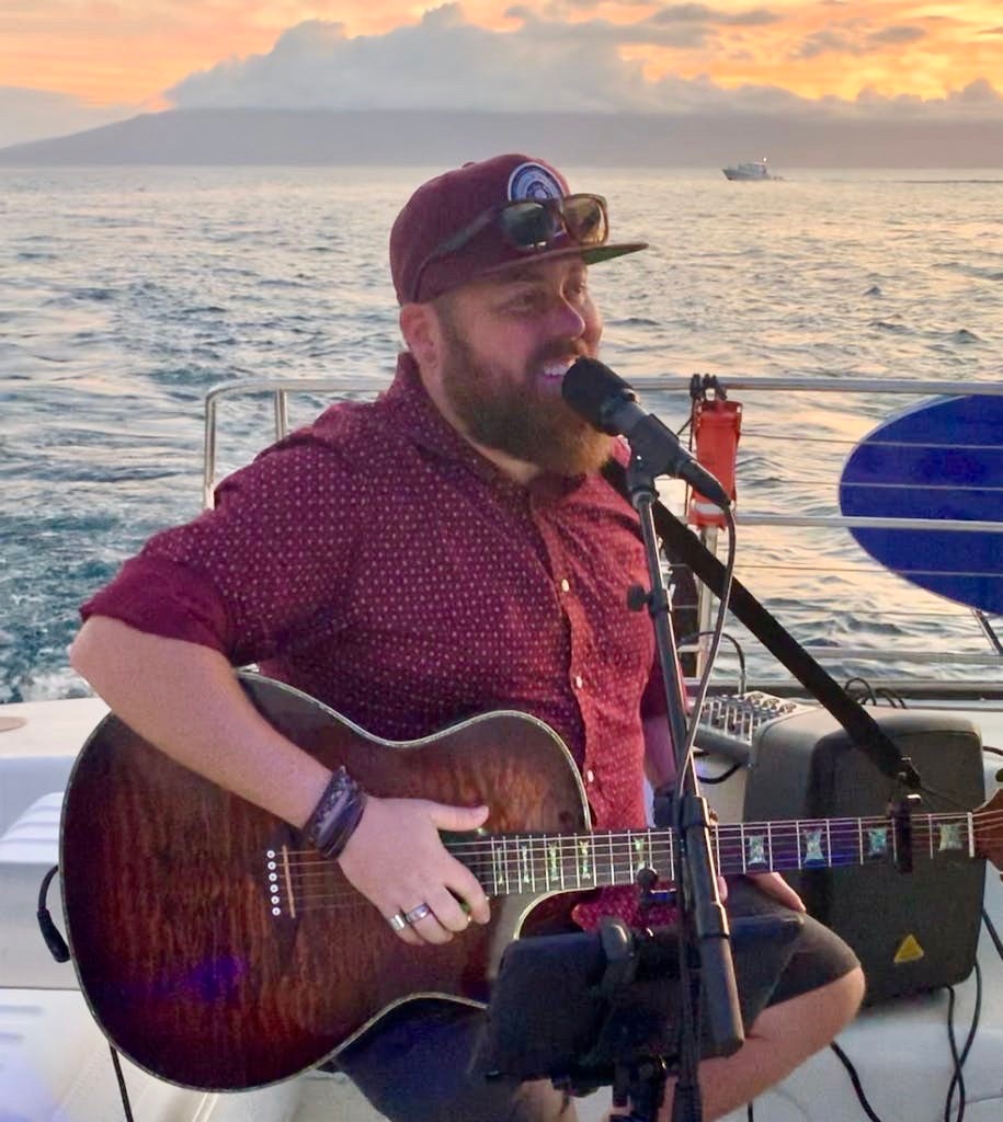 Man playing guitar and singing on a boat at sunset.