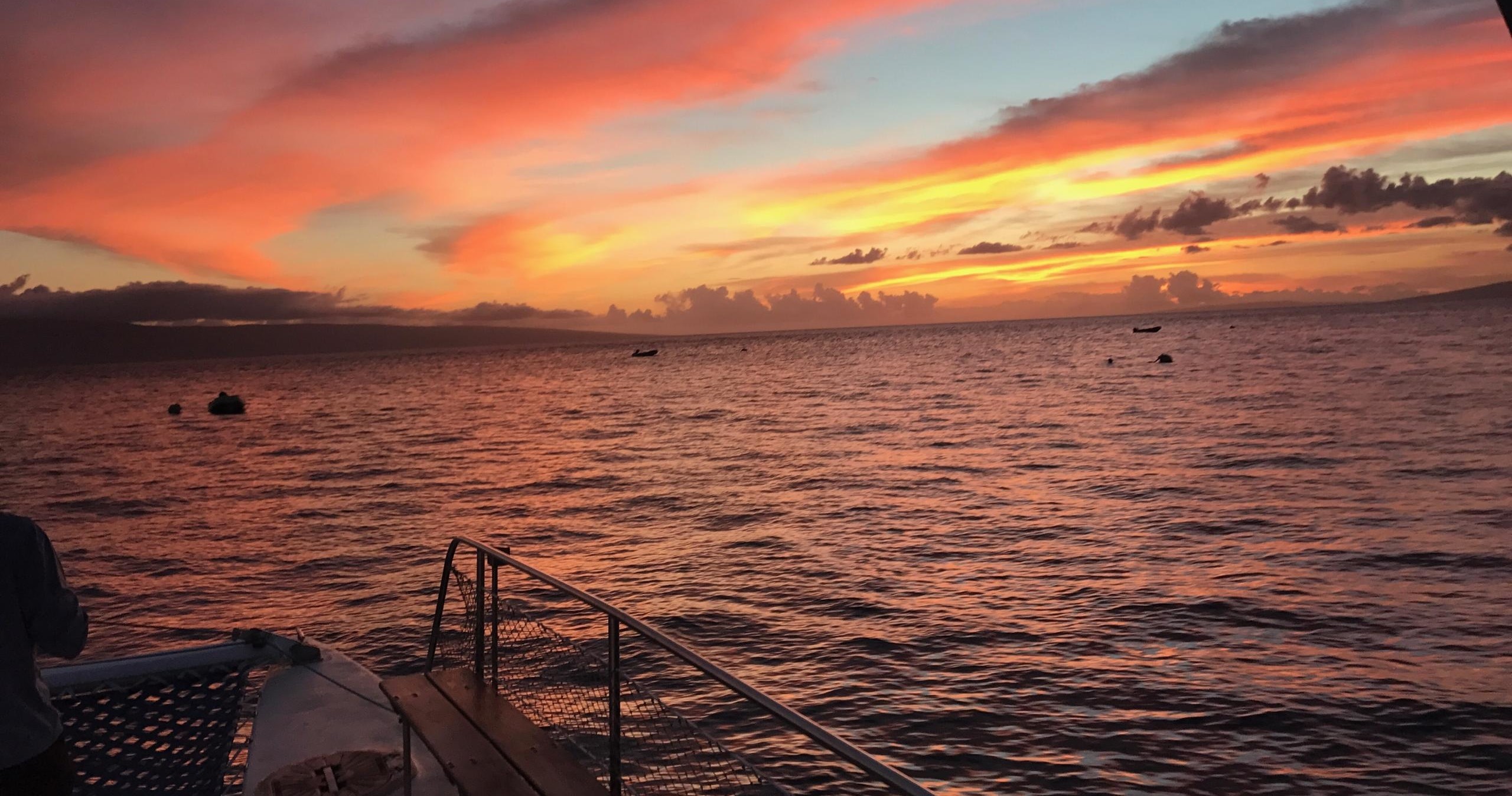 Sunset over a calm ocean with vibrant pink and orange clouds, seen from a boat.