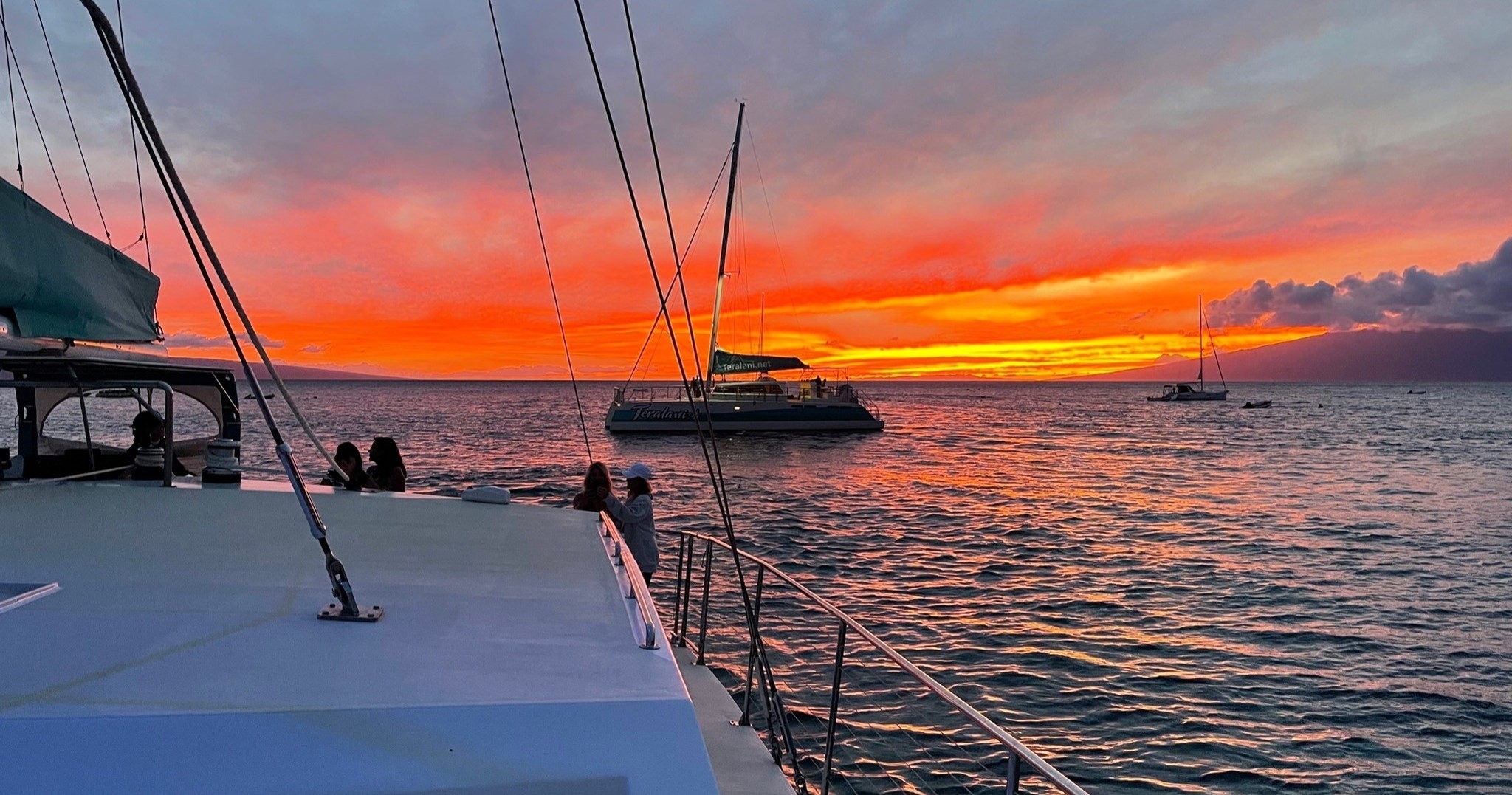 Sailboats on calm sea at sunset with vibrant orange sky.