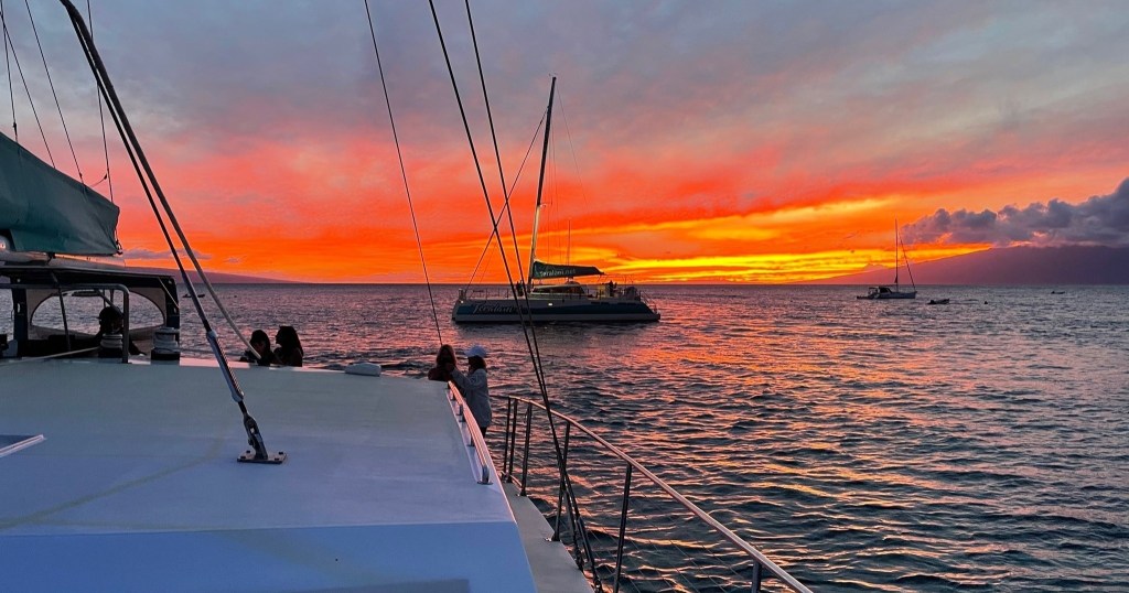 Sailboats on calm sea at sunset with vibrant orange sky.