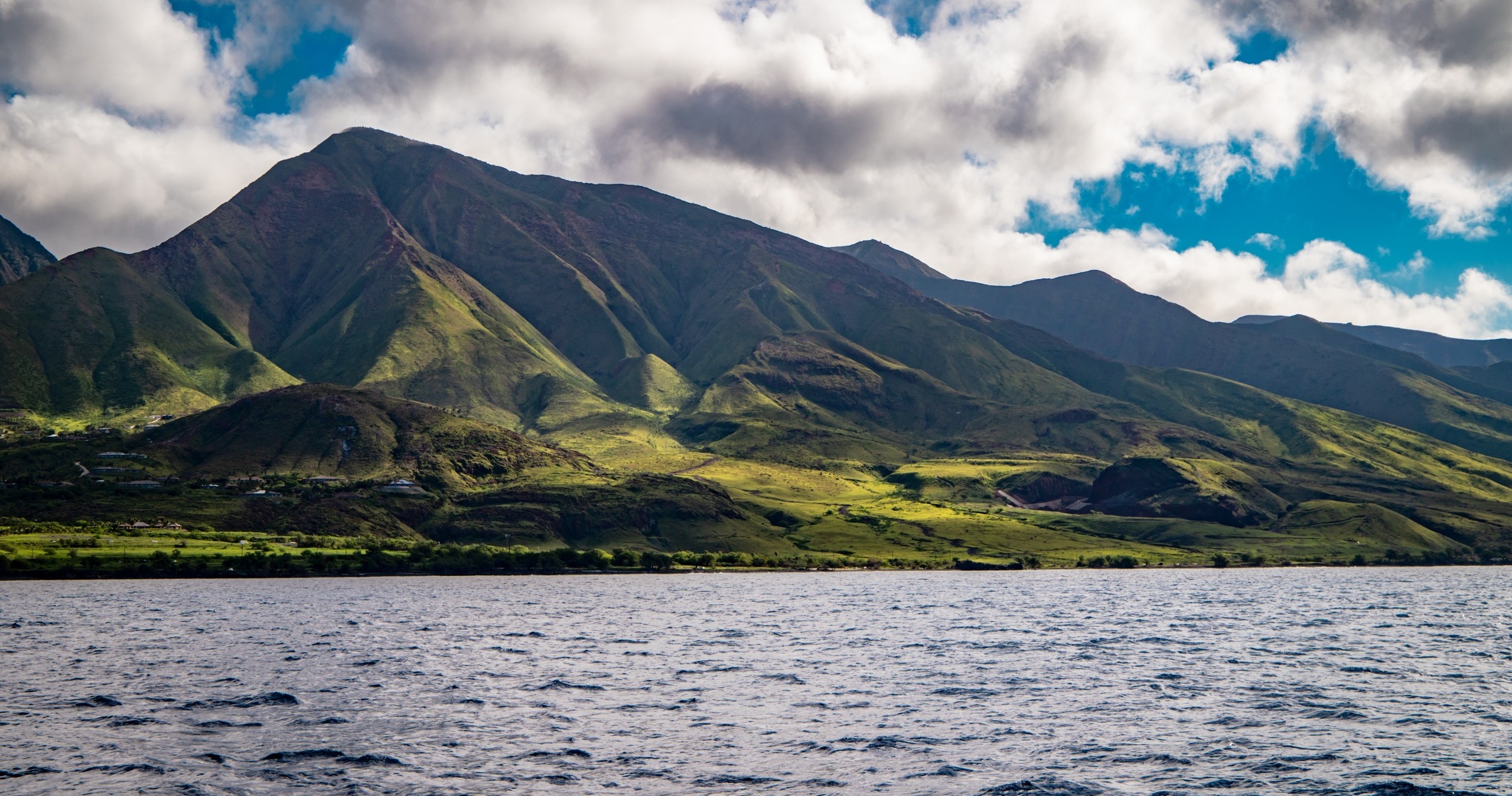 Mountain and lush greenery by the sea under a partly cloudy sky.