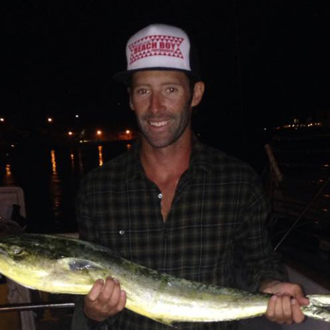 Man wearing a cap holding a fish at night.