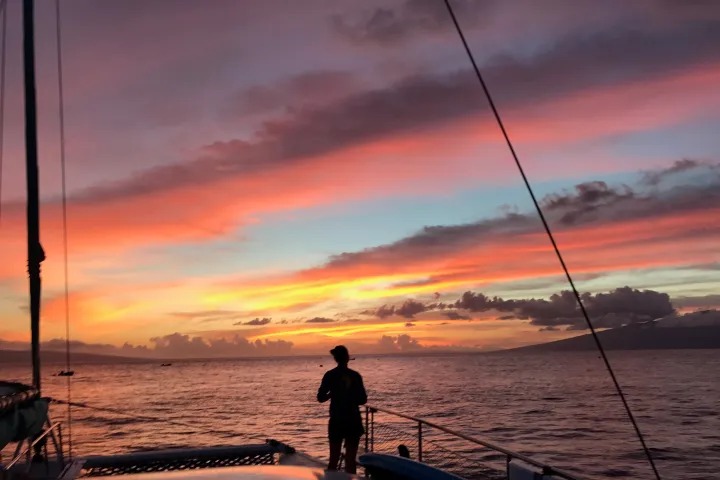 Person on a boat deck at sunset with a colorful sky and clouds.