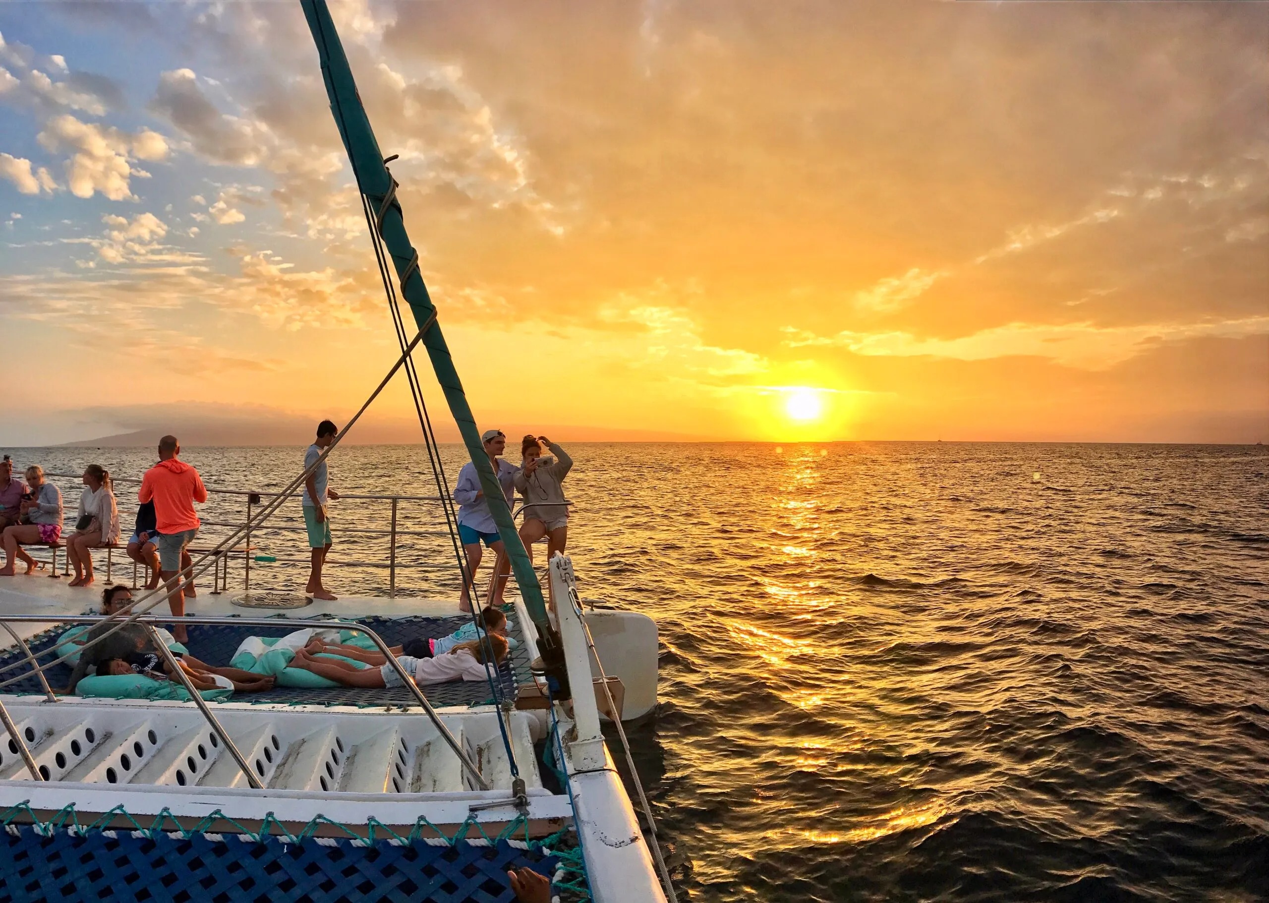 Group on a catamaran at sunset over the ocean.