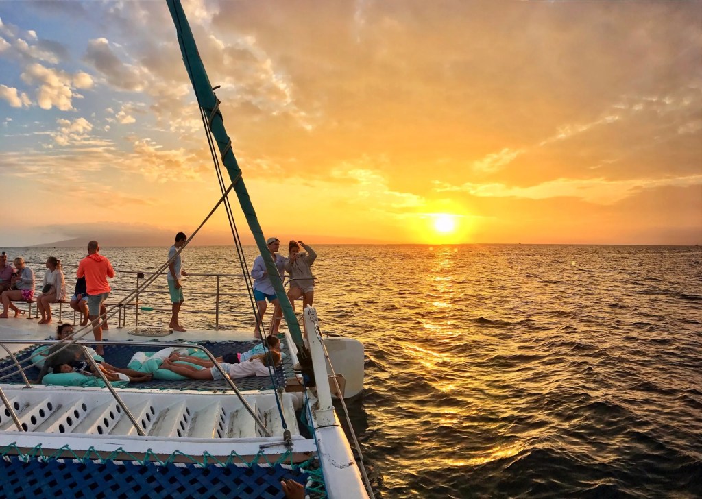 Group on a catamaran at sunset over the ocean.