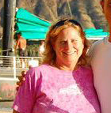 Two people smiling in front of a boat and mountainous landscape.