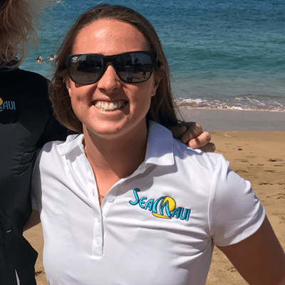 Woman in white Sea Maui shirt and sunglasses on a beach.