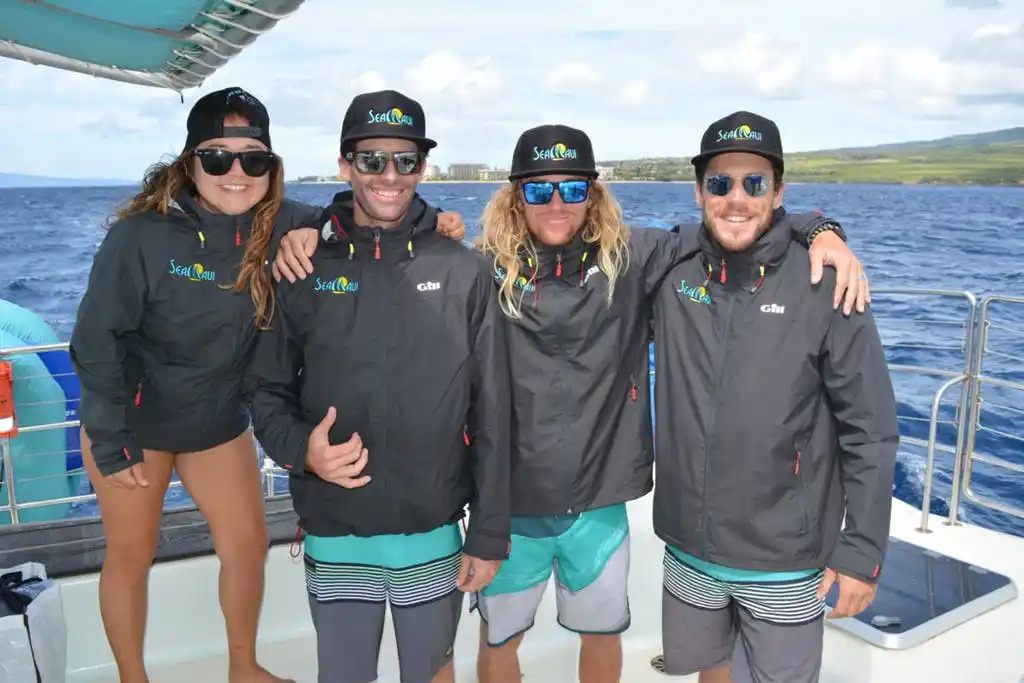 Four people in matching jackets and hats on a boat near the ocean.