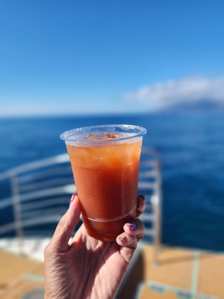 Hand holding orange drink in plastic cup by the sea.