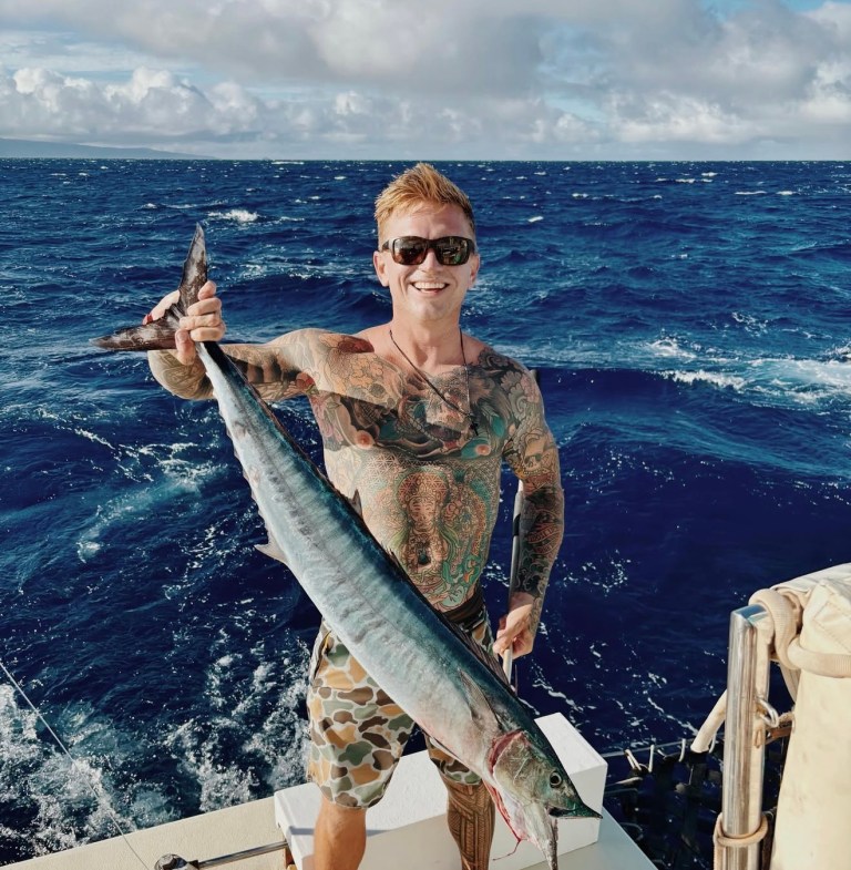 Smiling person with tattoos holding a large fish on a boat in the ocean.