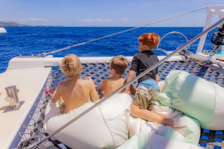 Three children sitting on a sailboat net over the ocean.