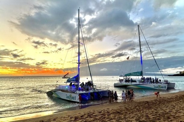 Two sailboats on the shore at sunset with people nearby.