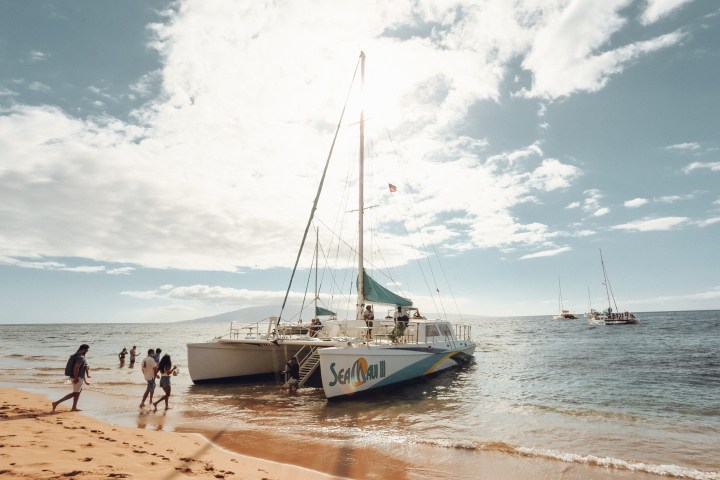 Catamaran on beach with people and distant sailboats, sunny day.