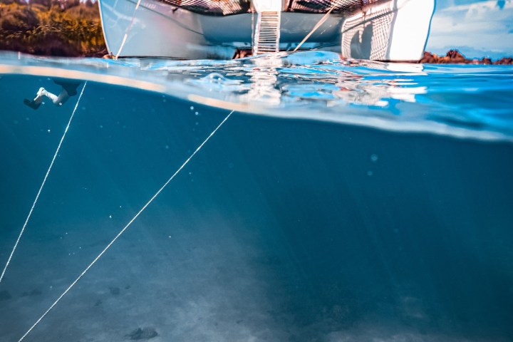Half-submerged view of a sailboat above a turtle swimming underwater.
